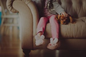 a small girl sitting on the sofa with a cute dog