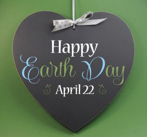 Happy Earth Day April 22, message sign greeting on a heart shaped blackboard against a green background.